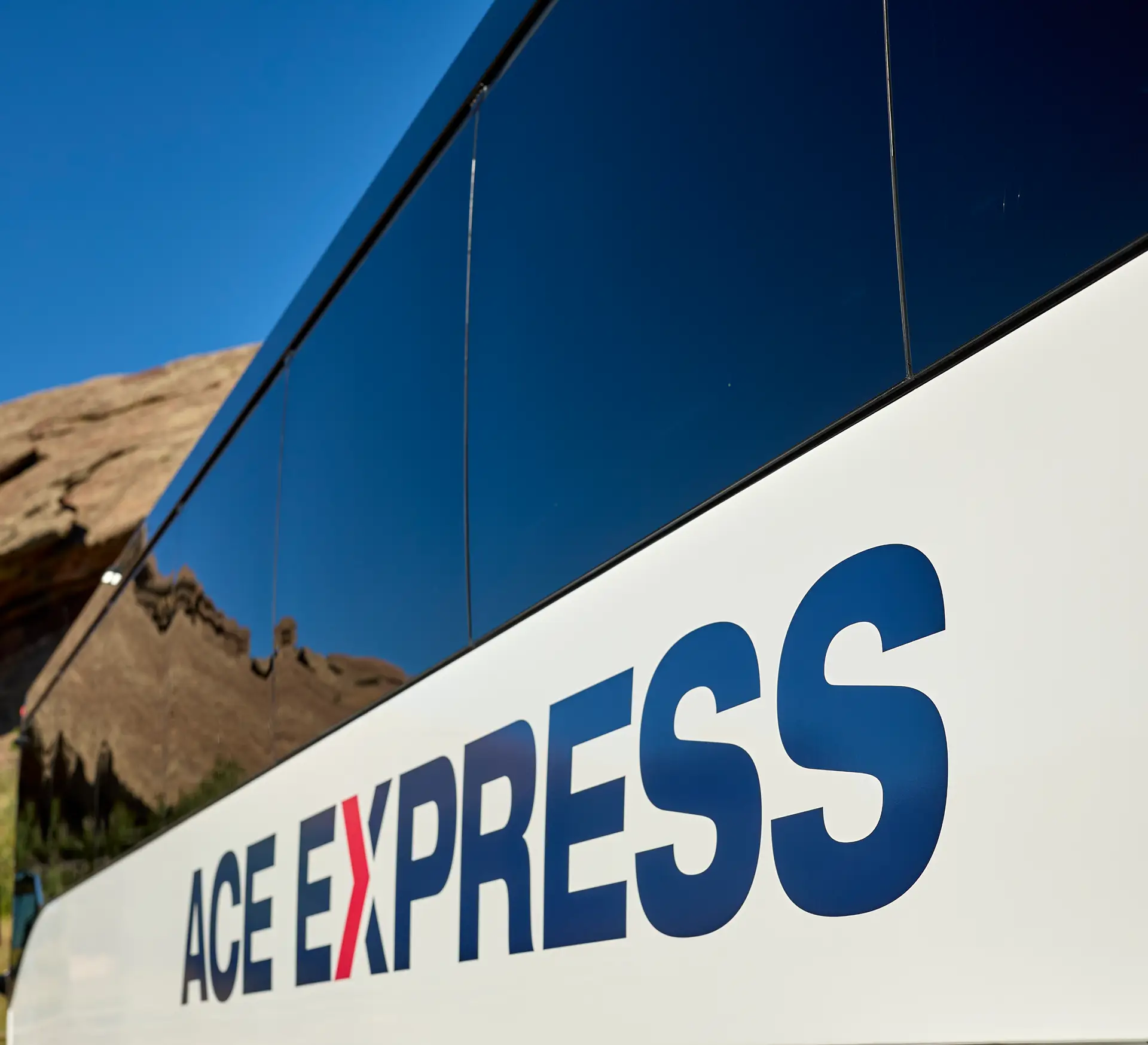 Ace Express Coaches logo displayed on the side of a motorcoach with a mountain background.