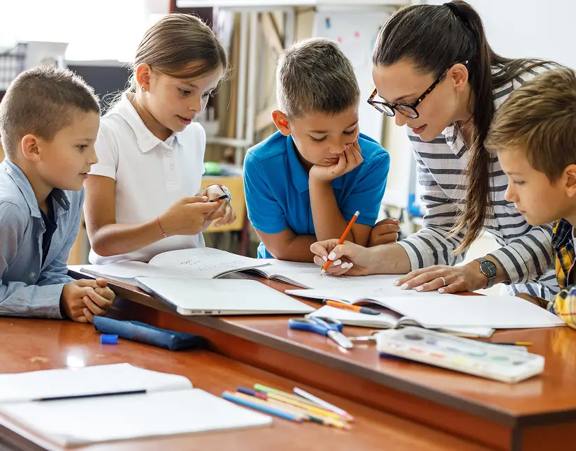 Children and teacher engaged in a learning activity at a classroom table.