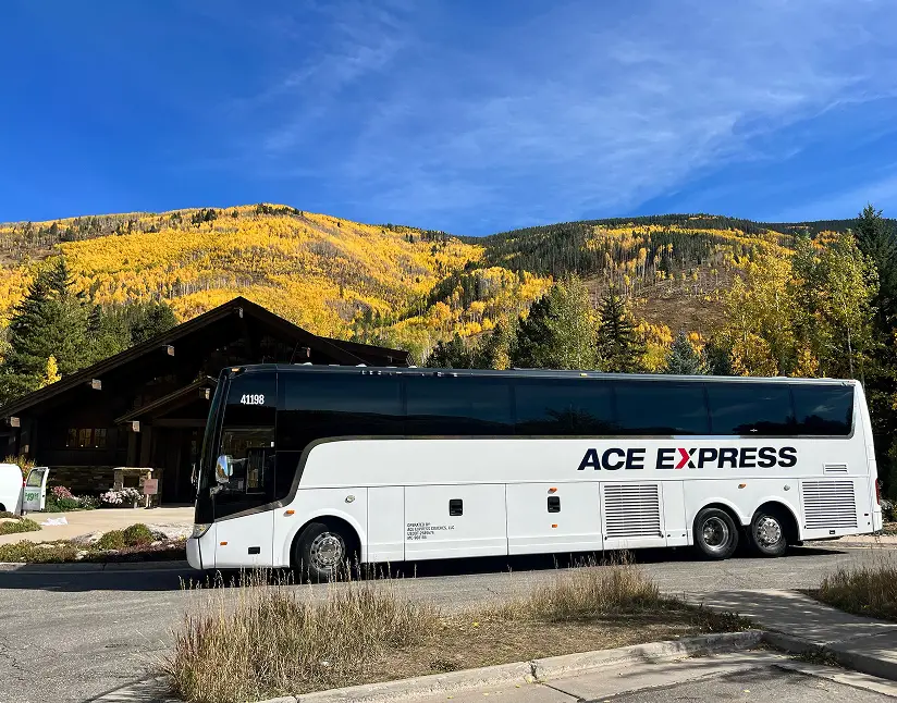 Luxury coach motorcoach parked outdoors with colorful fall foliage and mountains in the background.