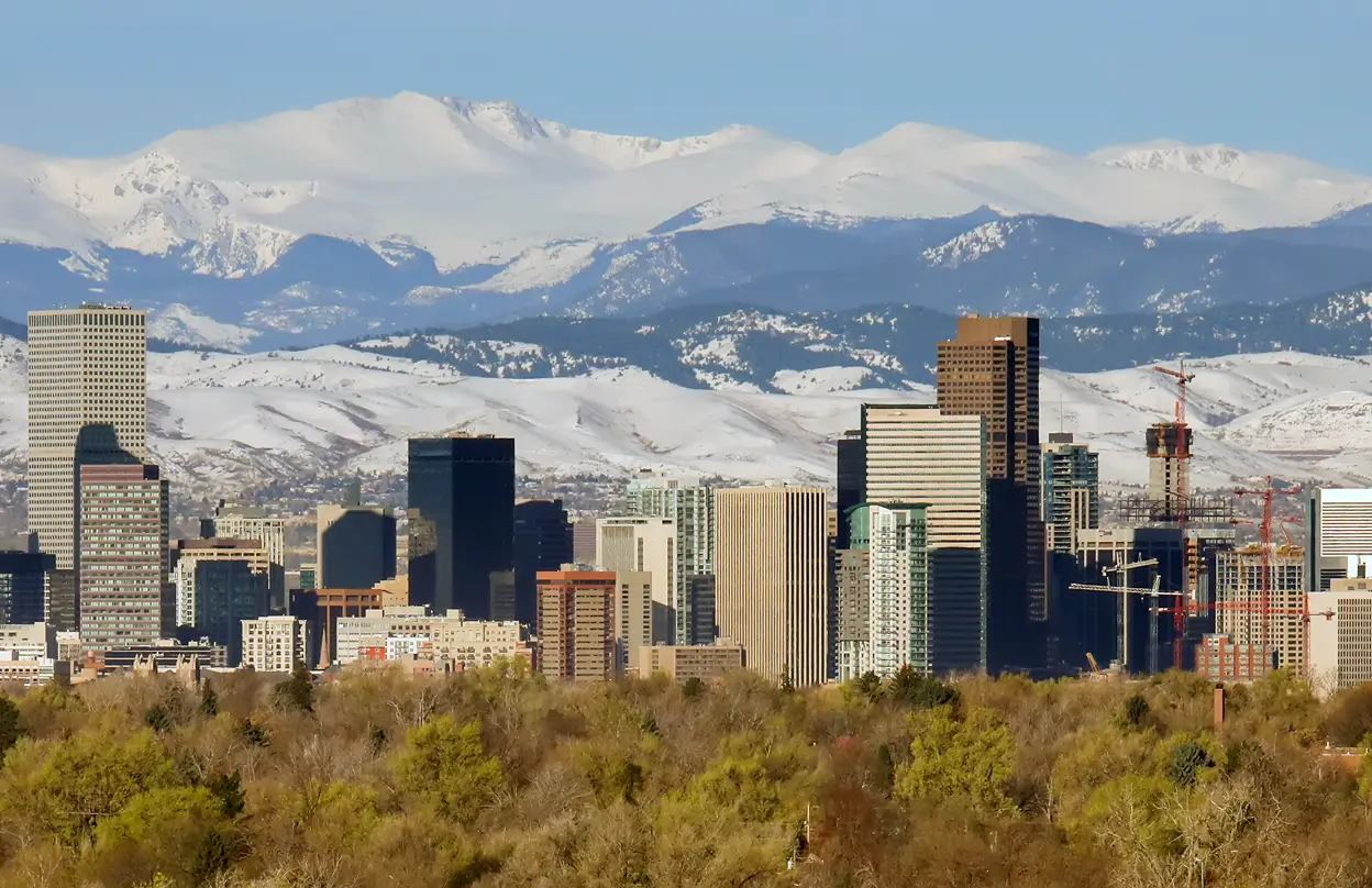 Denver cityscape with snow-covered mountains and skyscrapers.