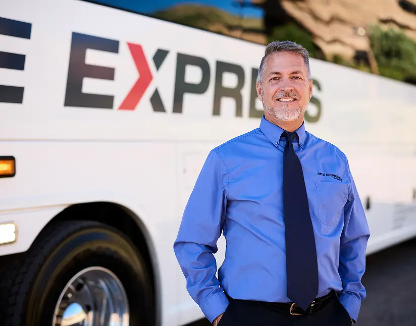 Motorcoach driver in uniform standing in front of Ace Express Coaches motorcoach.
