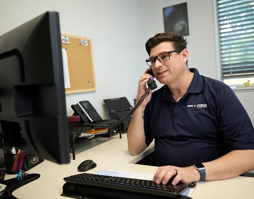 Customer service representative at Ace Express Coaches office using a phone and computer.