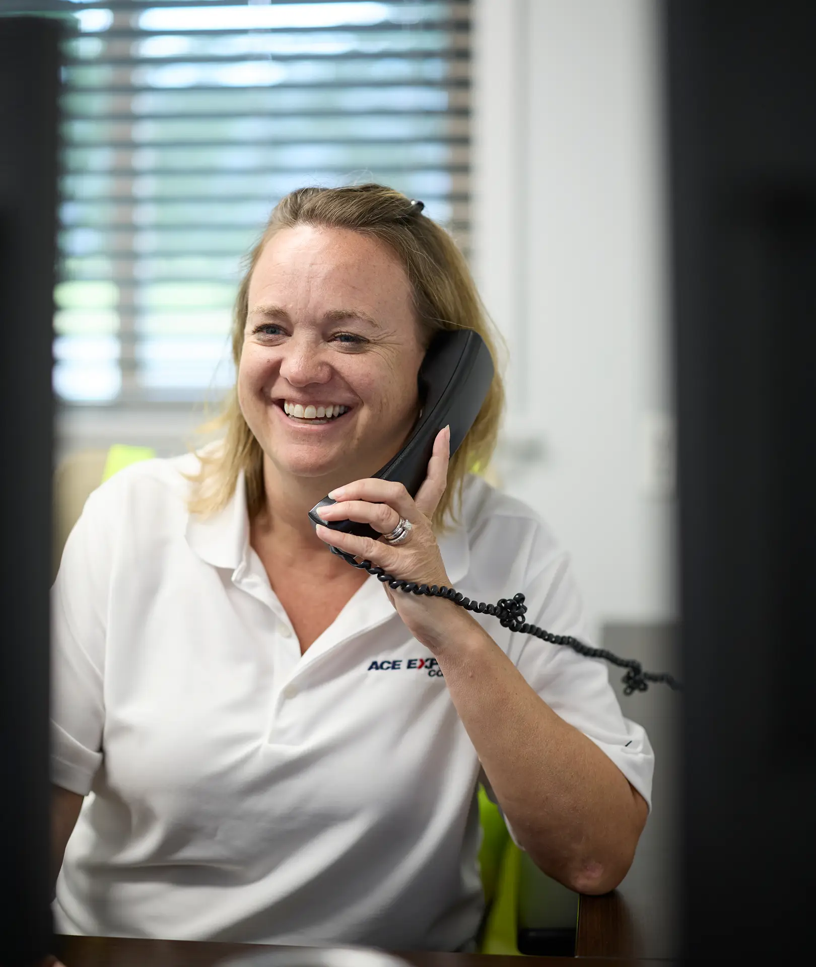 Smiling woman in uniform talking on a phone at Ace Express Coaches office.