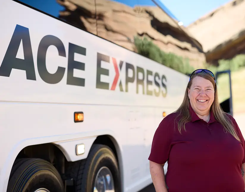 Motorcoach with Ace Express Coaches logo and a cheerful female employee standing beside it.