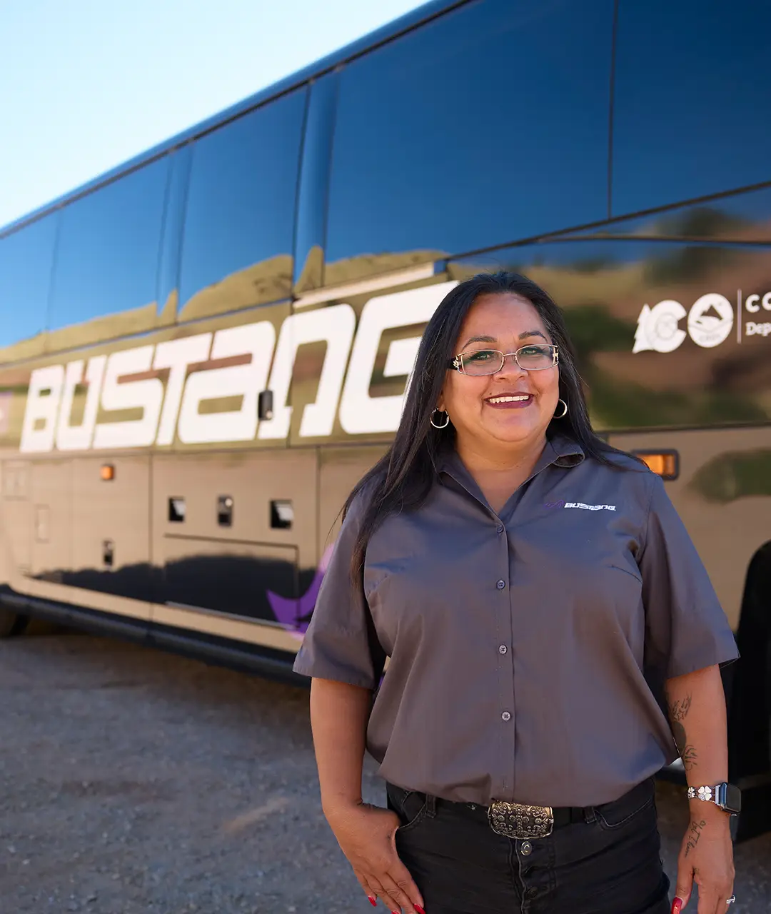 Smiling woman in uniform standing beside a sleek blue motorcoach.
