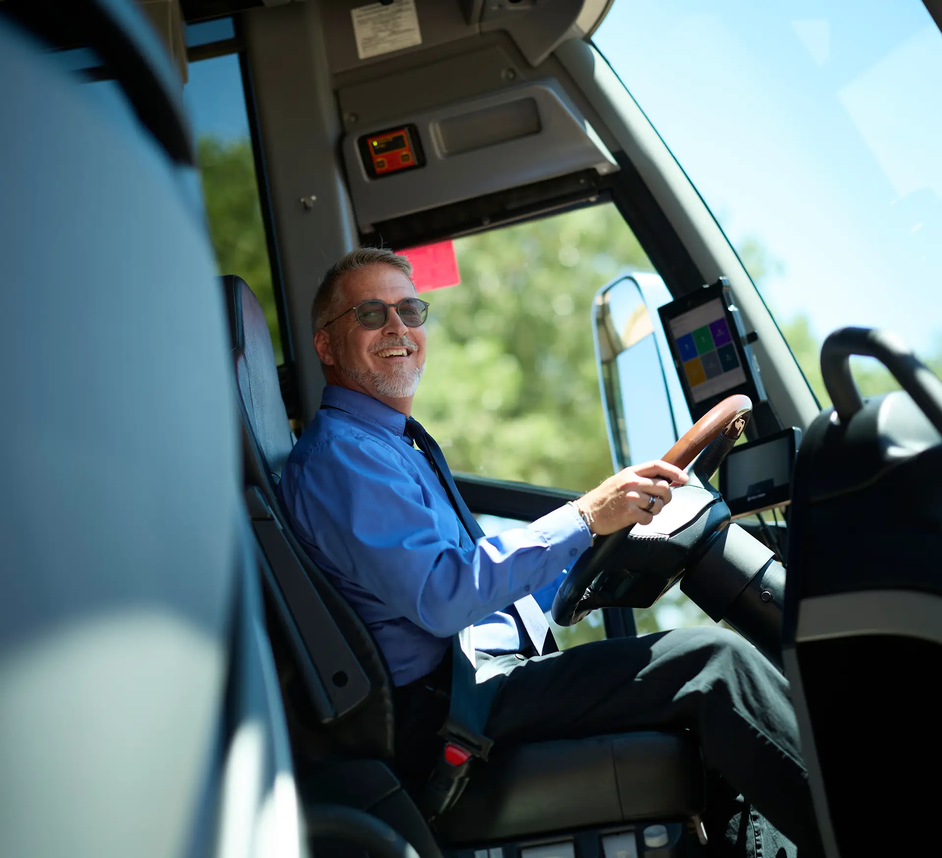 Experienced motorcoach driver smiling at the wheel of a coach.