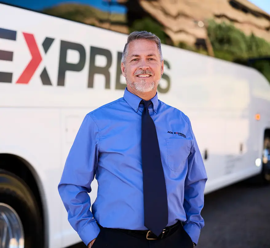 Friendly Ace Express Coaches driver standing in front of a white motorcoach with company logo.