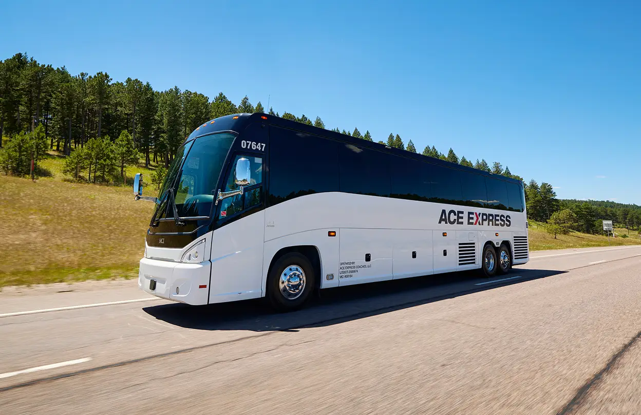 Modern white and black Ace Express Coaches motorcoach traveling on a highway with a scenic green landscape.