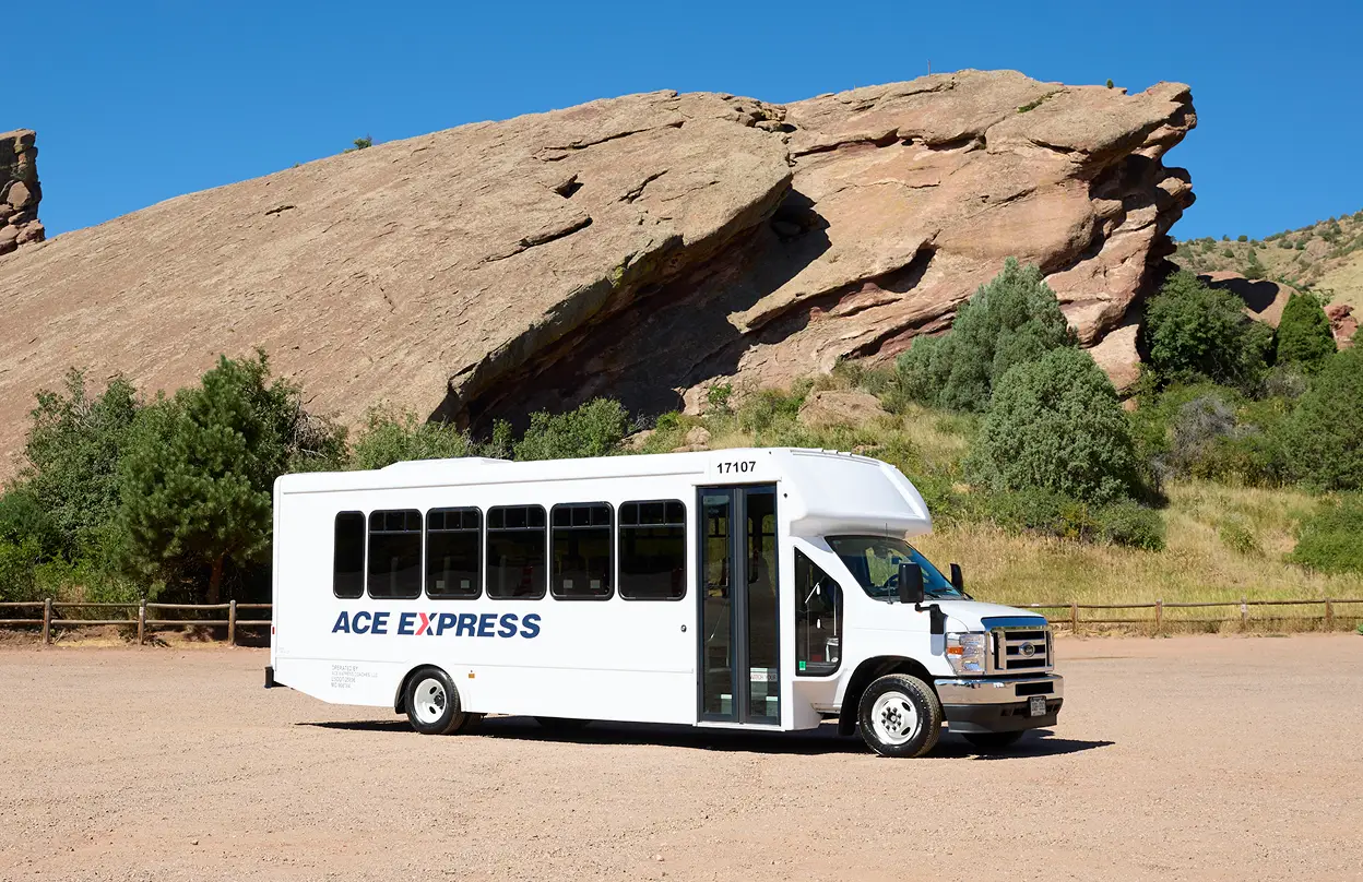 White Ace Express Coaches motorcoach parked outdoors with rocky landscape and blue sky.