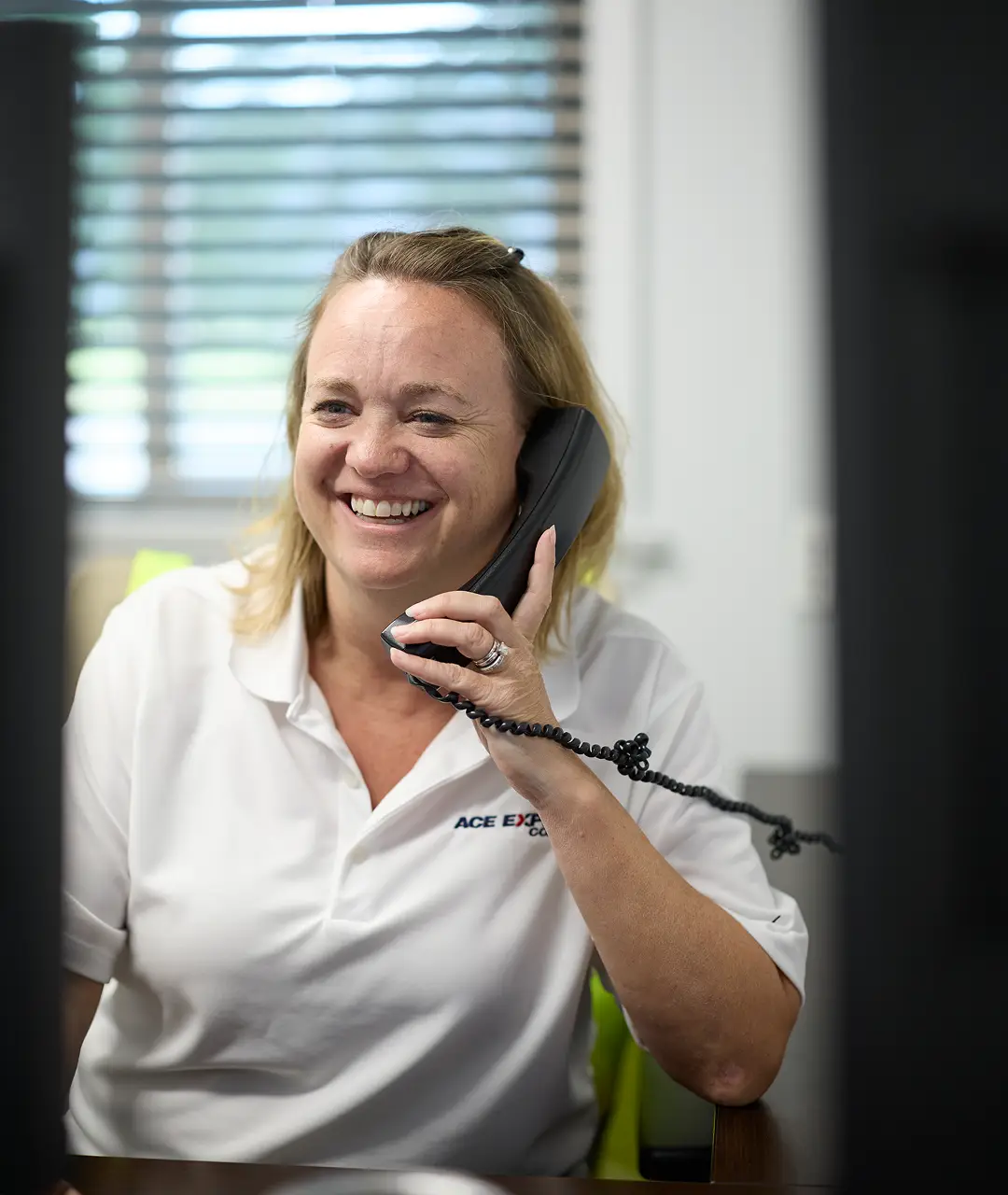 Smiling woman in uniform talking on a phone at Ace Express Coaches office.