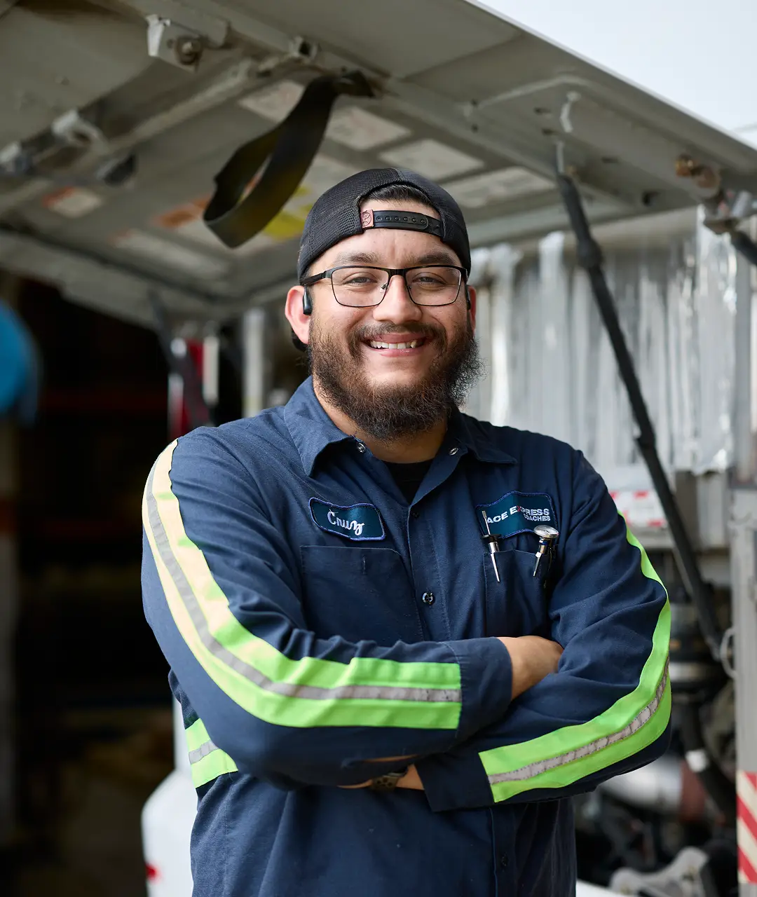 Technician smiling in uniform with arms crossed at motorcoach maintenance facility.