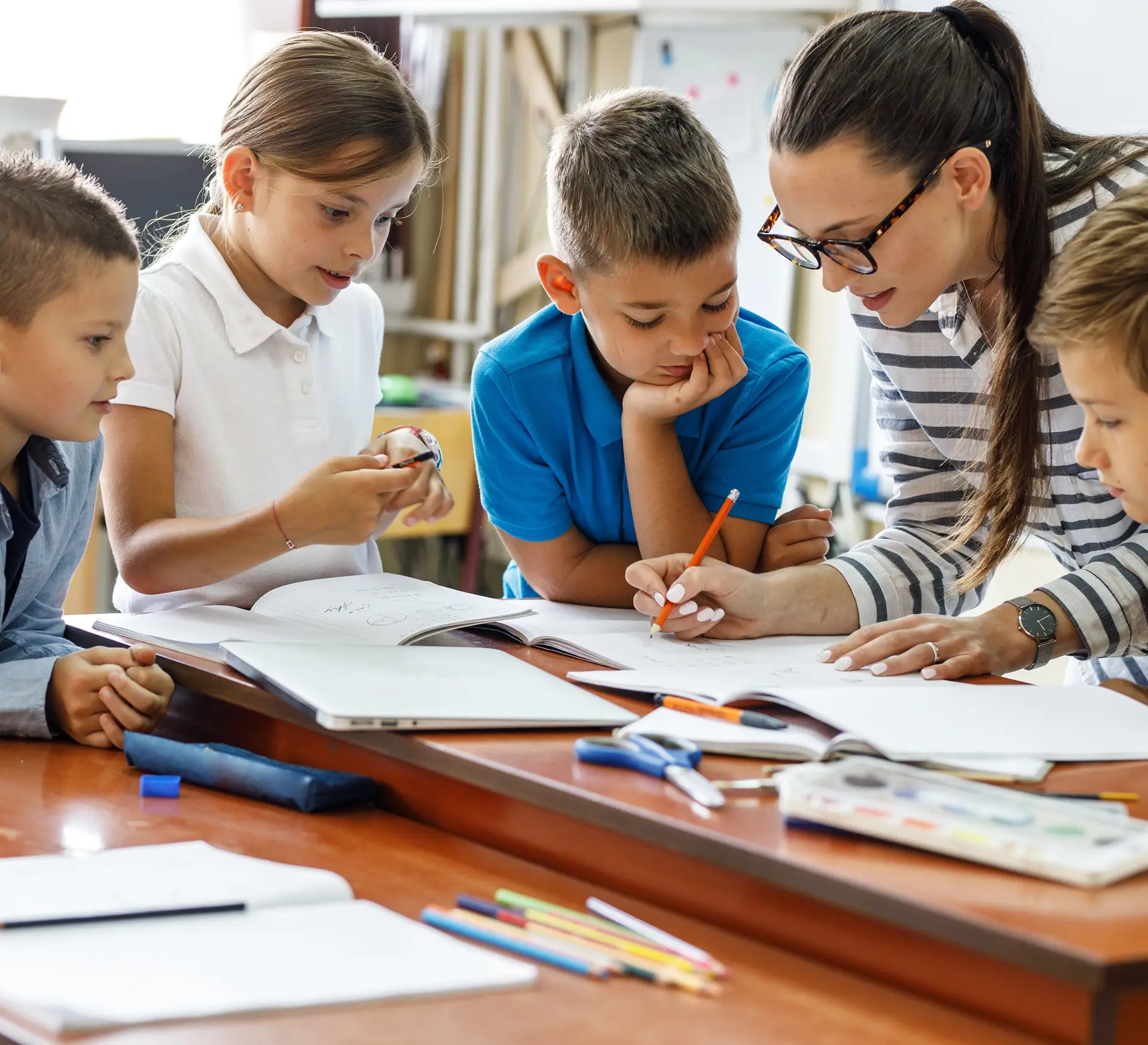 Teacher helping students with schoolwork and reading in classroom.