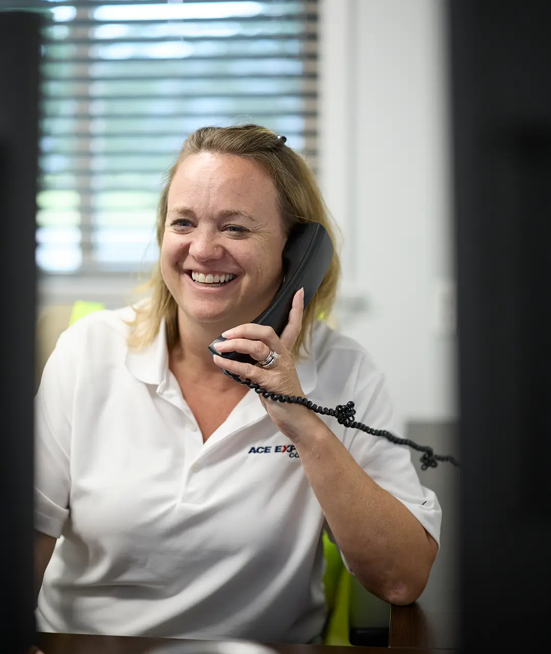 Smiling woman in white uniform talking on a landline phone at work.