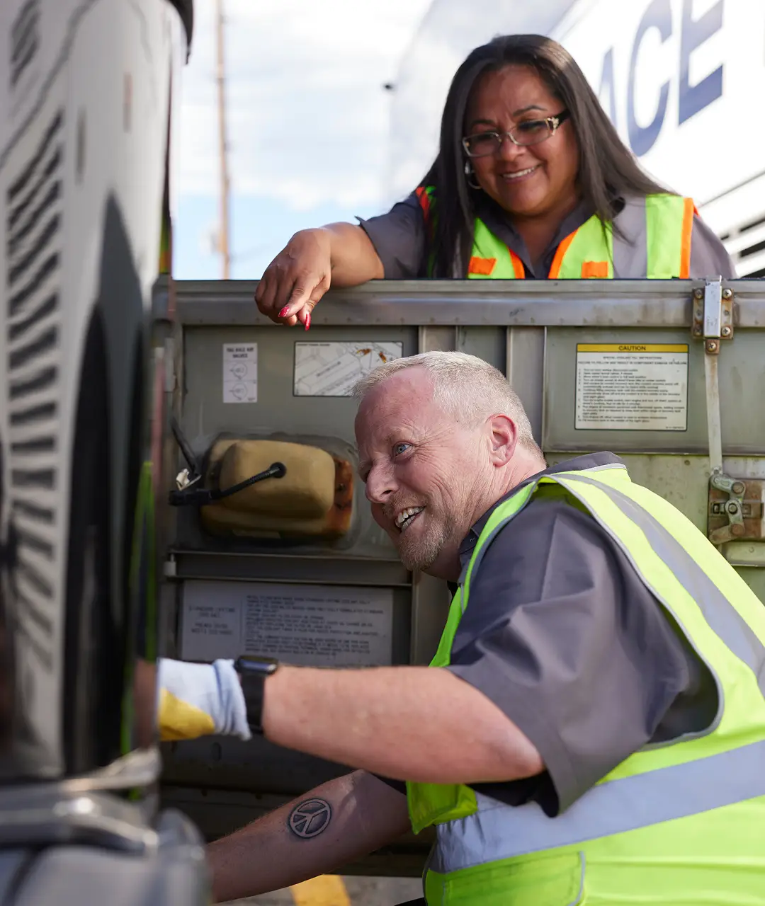 Two motorcoach maintenance workers, a woman and a man, inspecting and working on a motorcoach engine.