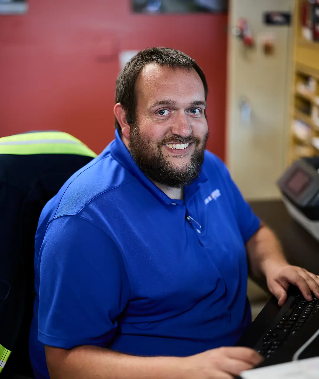 Friendly staff member at Ace Express Coaches working at a desk with a computer.