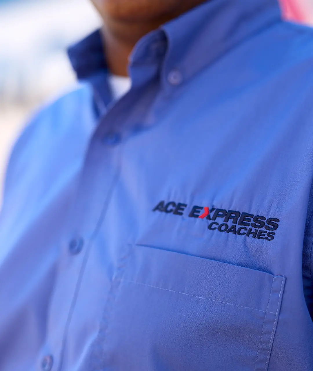 Close-up of Ace Express Coaches employee wearing a blue uniform shirt with logo.