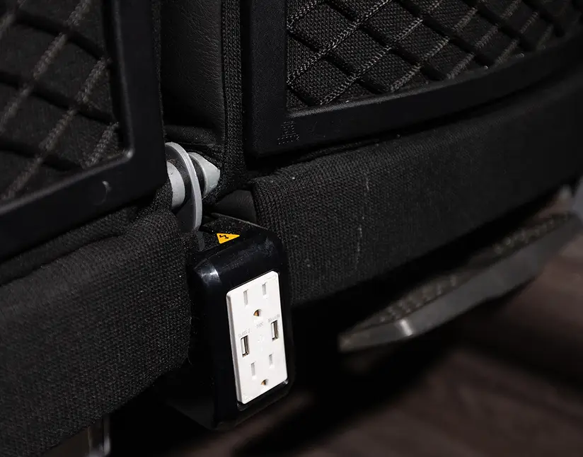 Power outlet attached to the back of a motorcoach seat for passenger convenience.