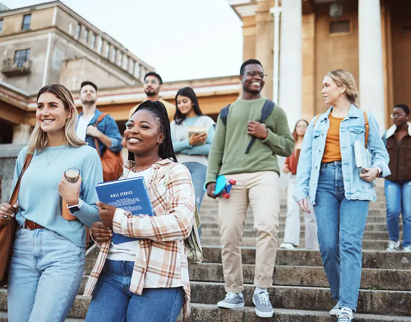Group of diverse students walking down university steps, smiling and chatting.