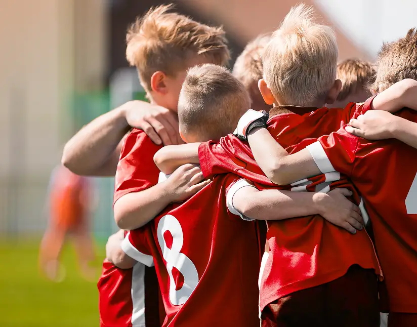 Group of young soccer players in red jerseys hugging after a game.