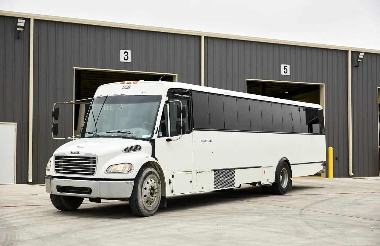 White and black passenger motorcoach parked outside a garage with numbered bays.