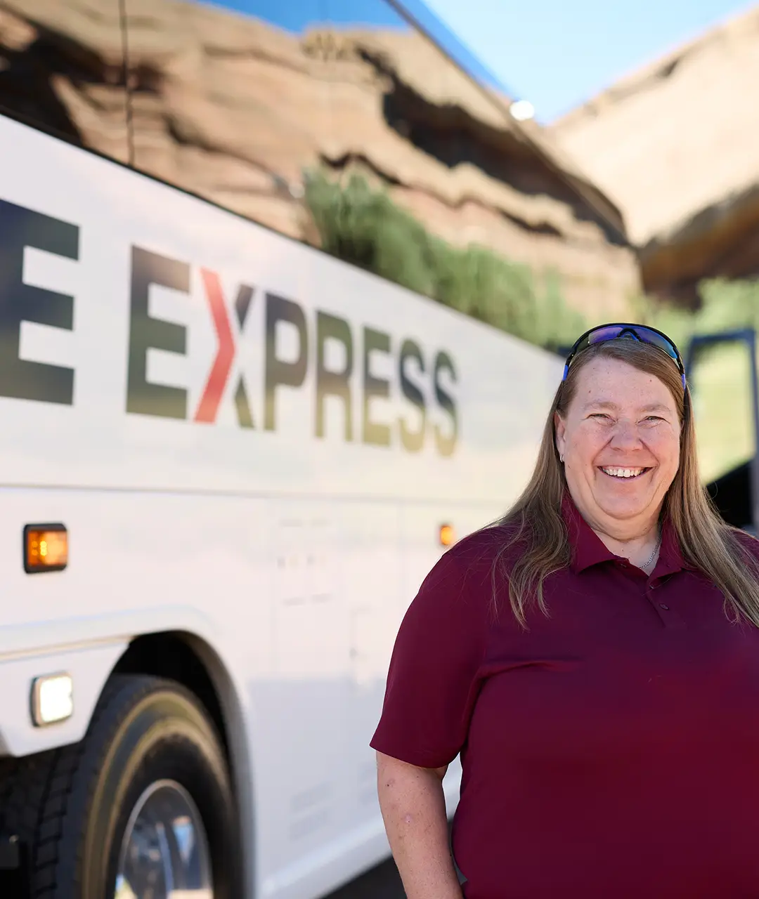 Motorcoach with Ace Express Coaches logo and a cheerful female employee standing beside it.
