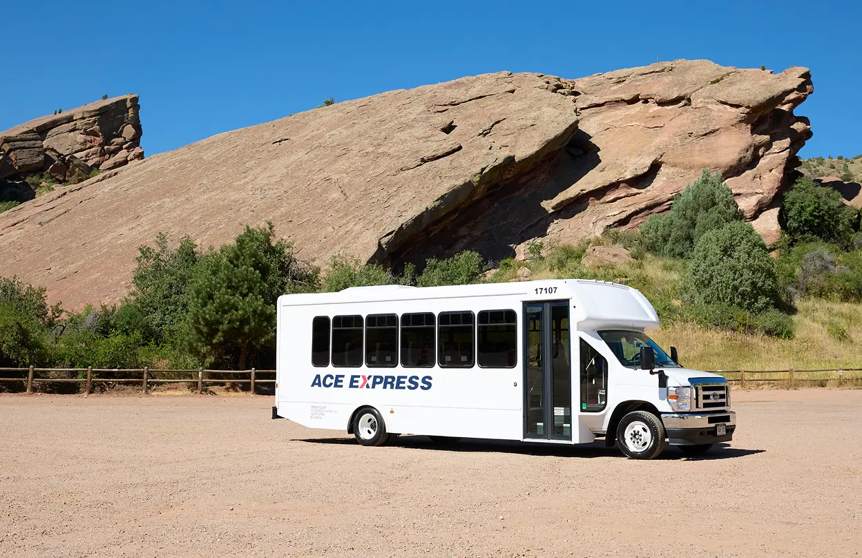 White Ace Express Coaches motorcoach parked outdoors with rocky landscape and blue sky.
