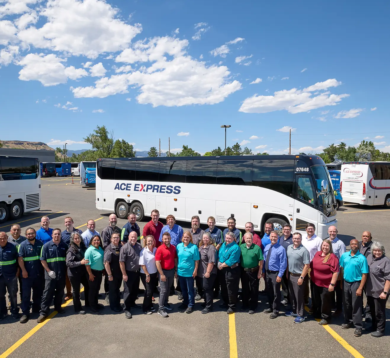 Group of Ace Express Coaches employees standing in front of a large motorcoach outdoors on a sunny day.