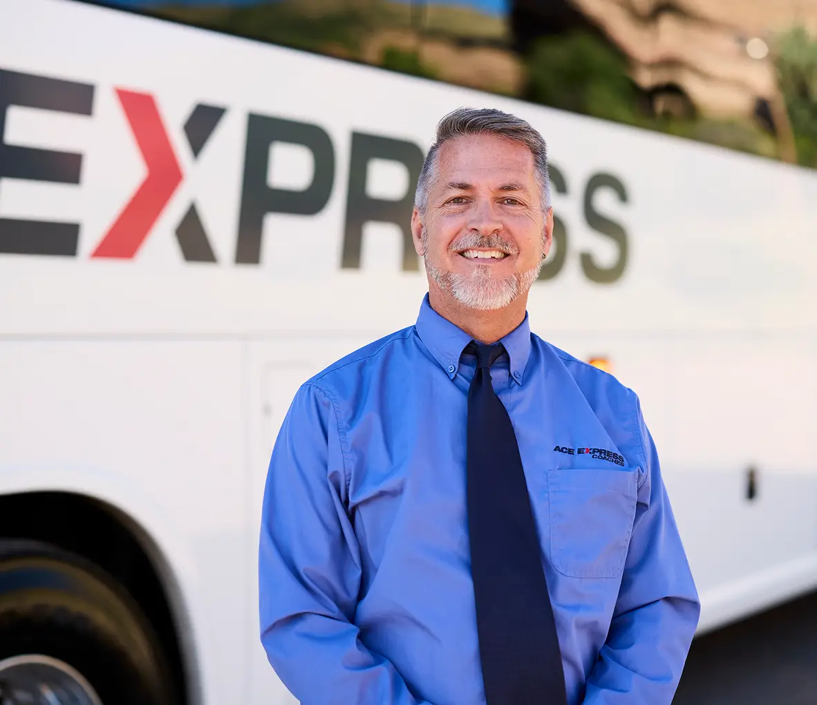 Friendly driver in uniform standing in front of Ace Express Coaches motorcoach.