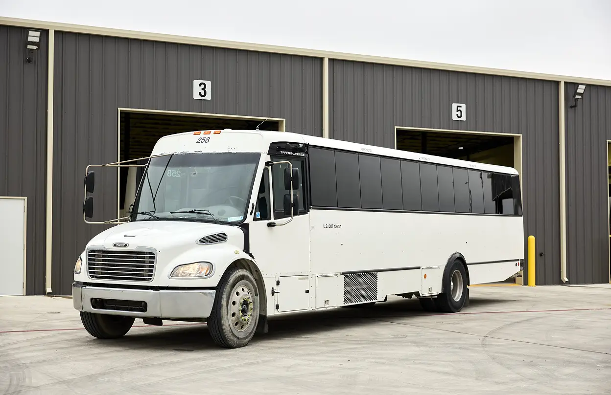 White passenger motorcoach parked outside a large industrial garage at Ace Express Coaches.