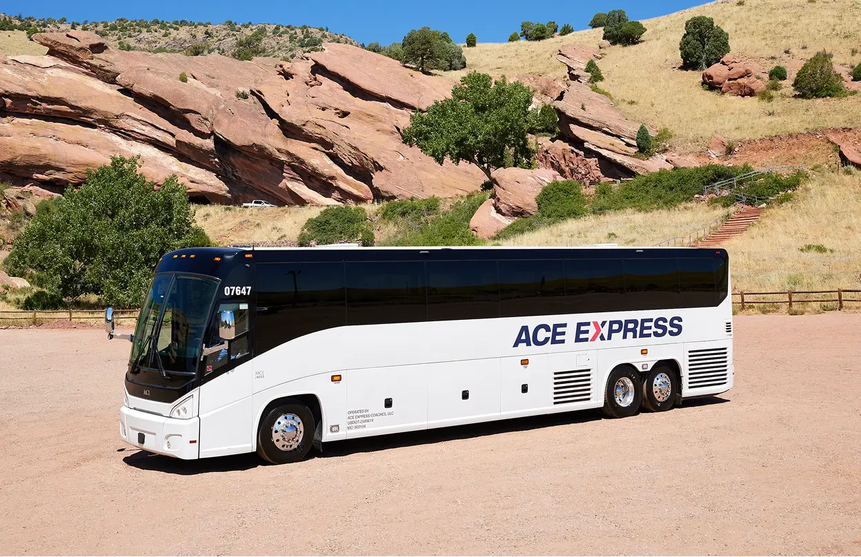 Modern white and black Ace Express Coaches motorcoach parked outdoors with rocky hills in the background.