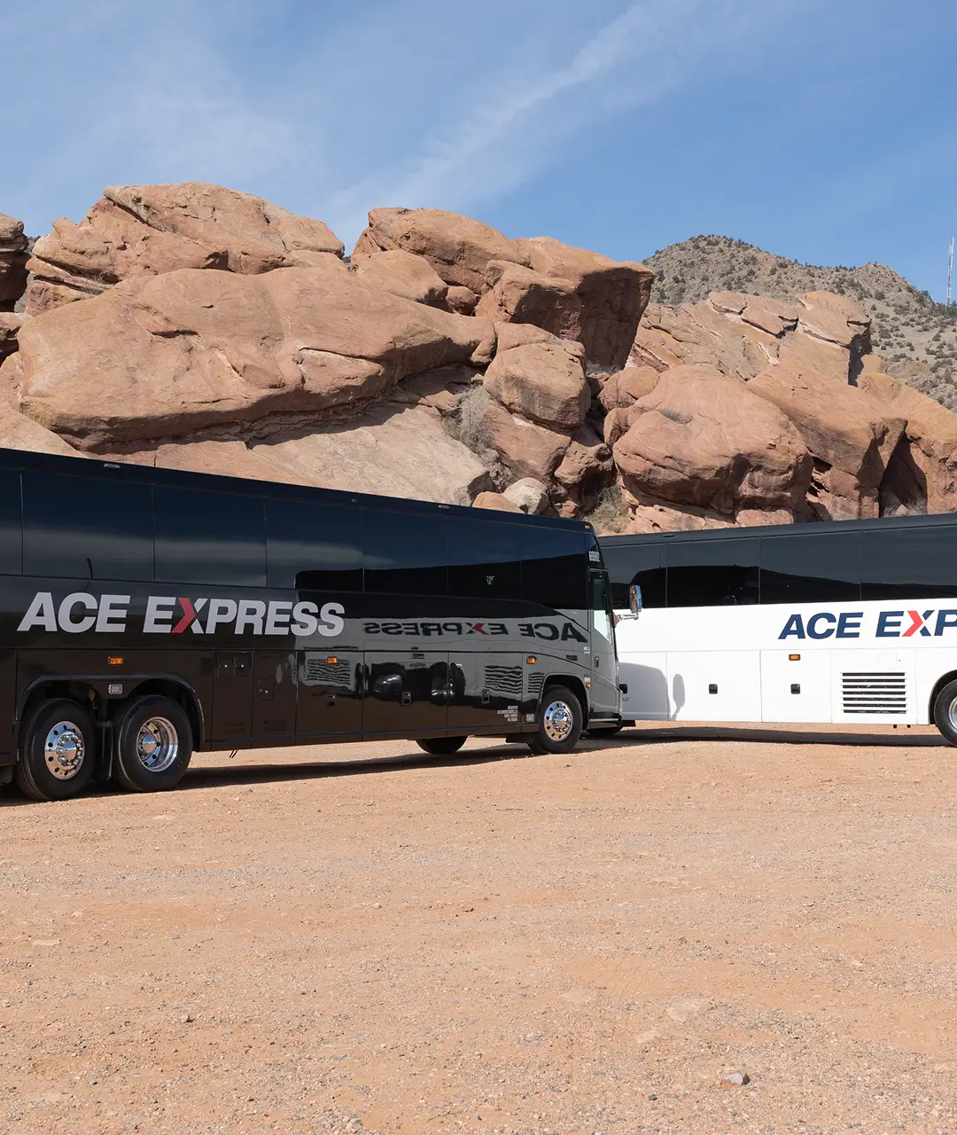 Two Ace Express Coaches motorcoaches parked on a dirt area with rocky hills in the background.