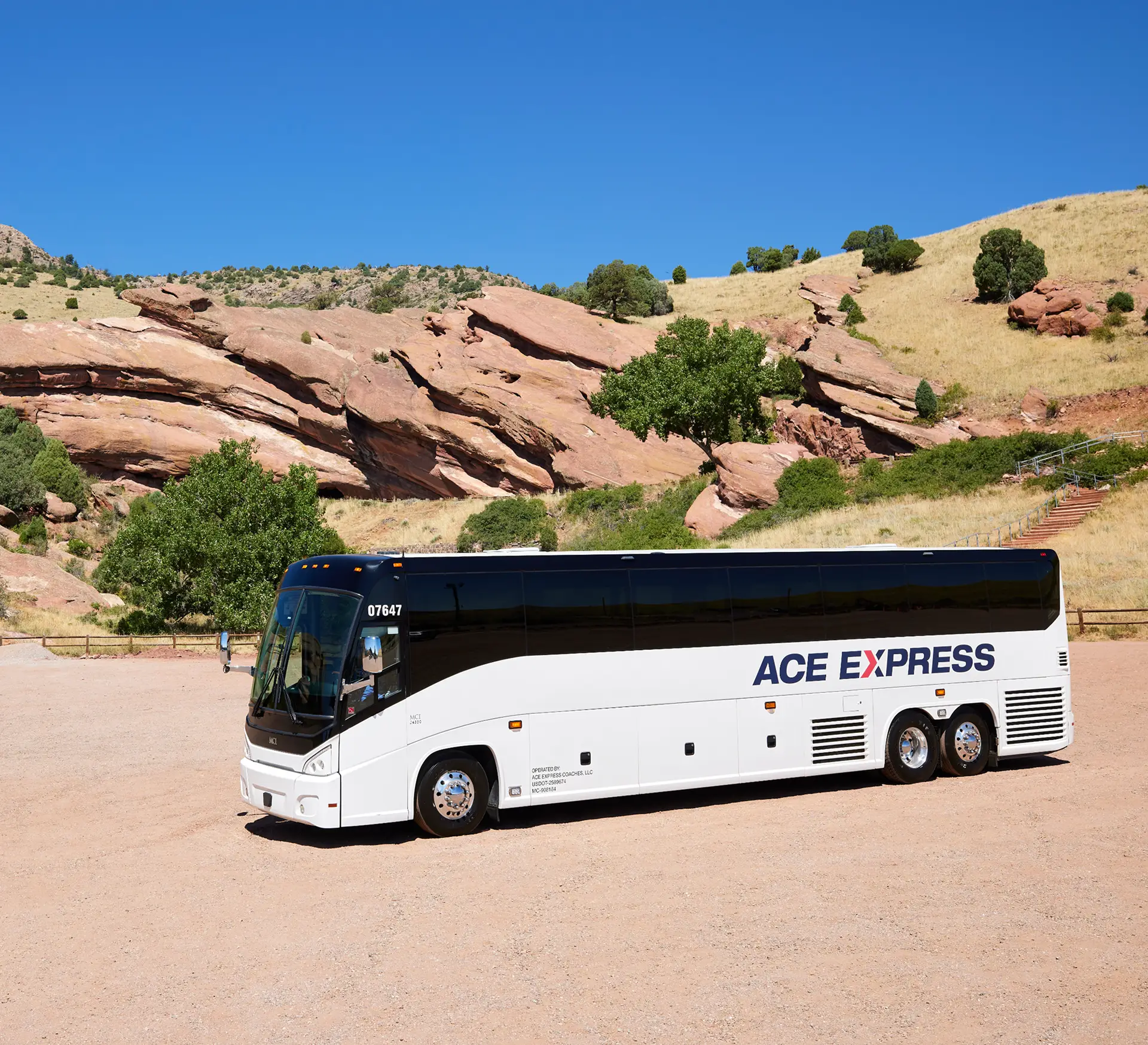 Modern white and black motorcoach with Ace Express logo parked in rocky desert landscape under clear blue sky.