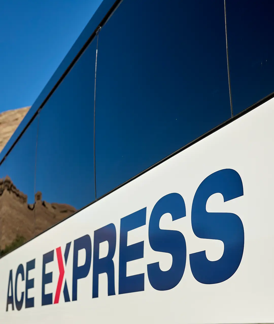 Modern motorcoach with Ace Express Coaches logo parked against a clear blue sky.