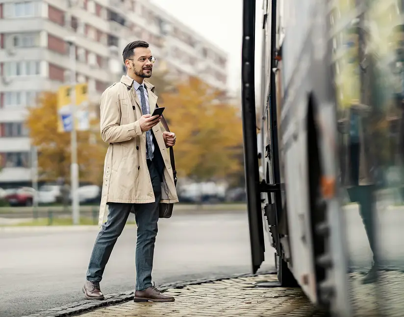Man using smartphone while boarding Ace Express Coaches motorcoach in an urban setting.