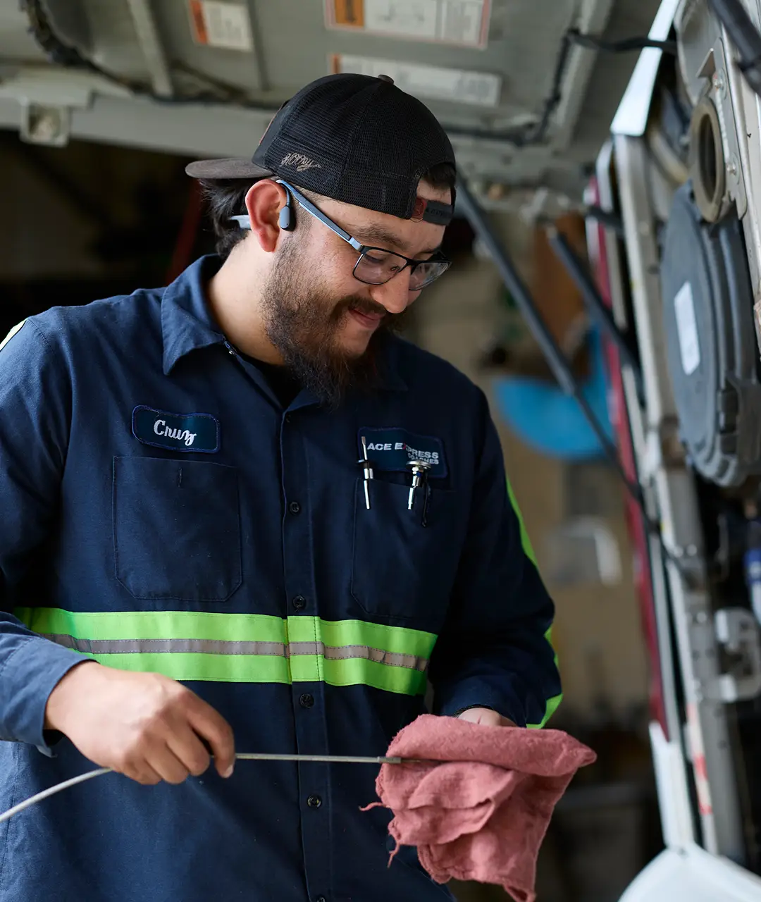 Motorcoach maintenance technician inspecting or repairing a motorcoach engine, wearing uniform and safety gear.