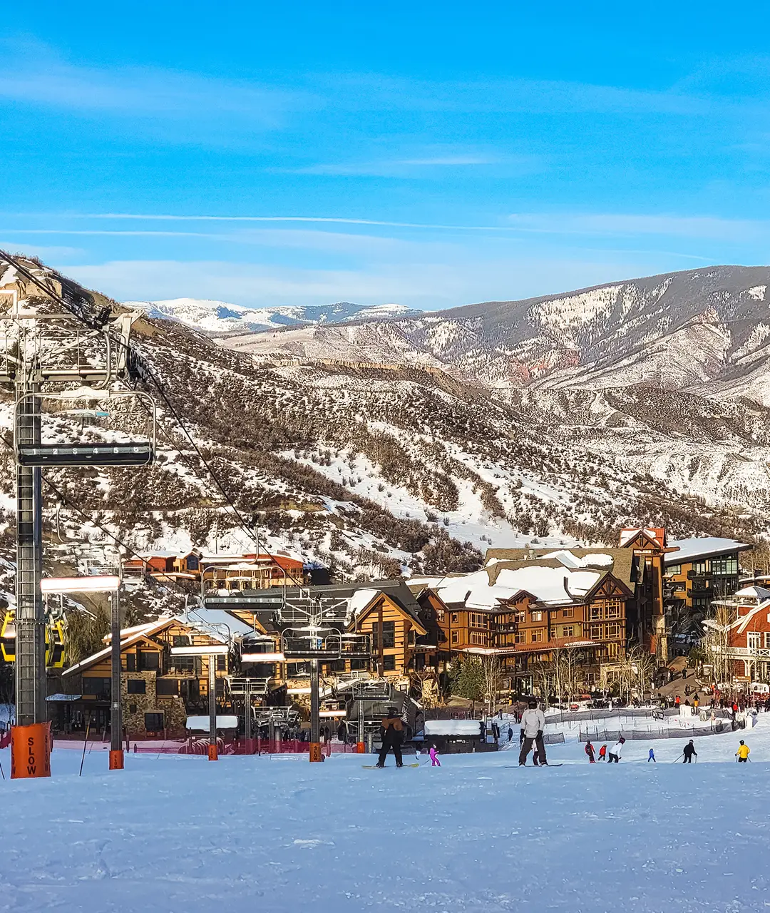 Scenic view of snow-covered mountains and ski resort with buildings and skiers.
