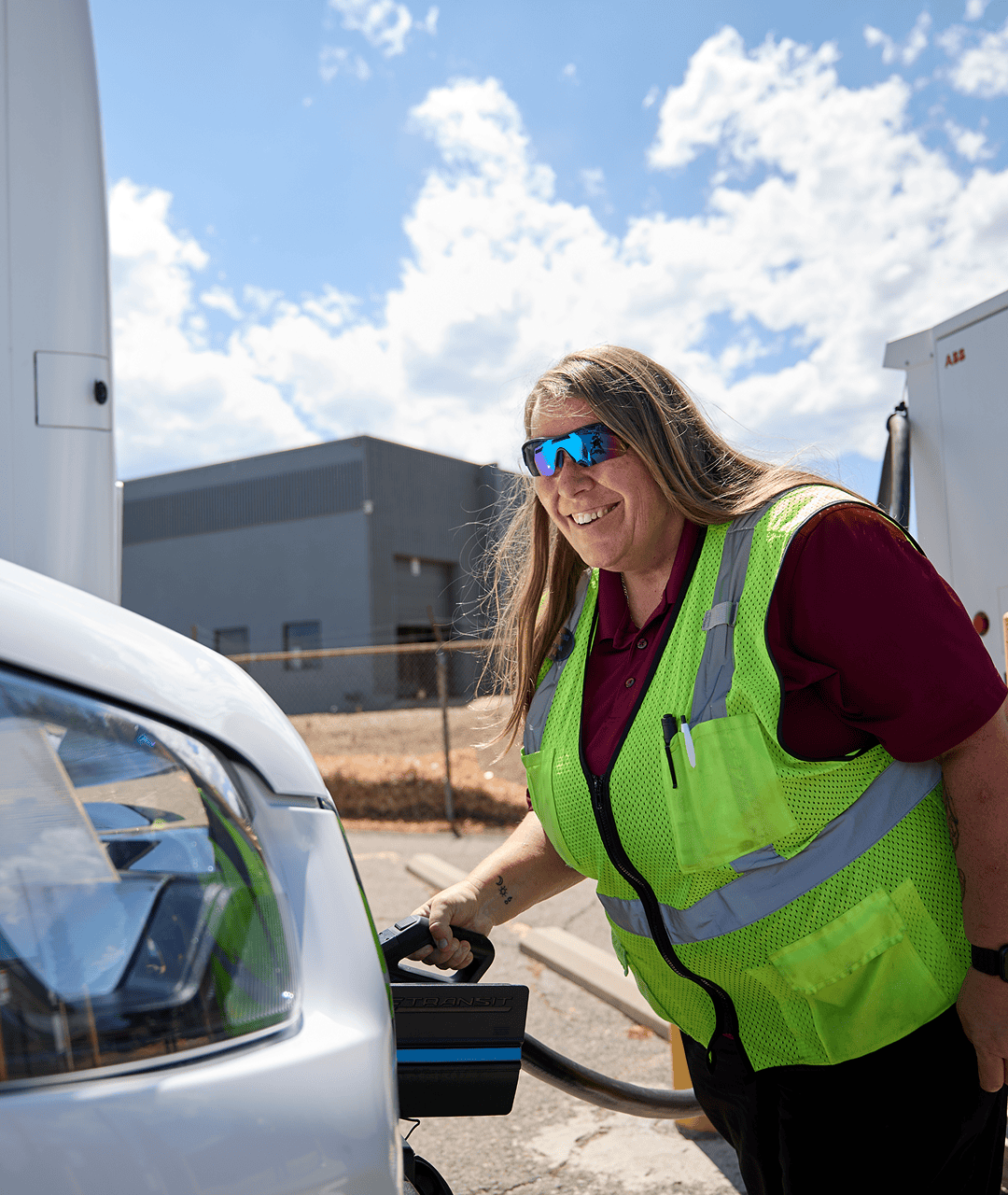 Female driver in safety vest charging an electric vehicle at a station.