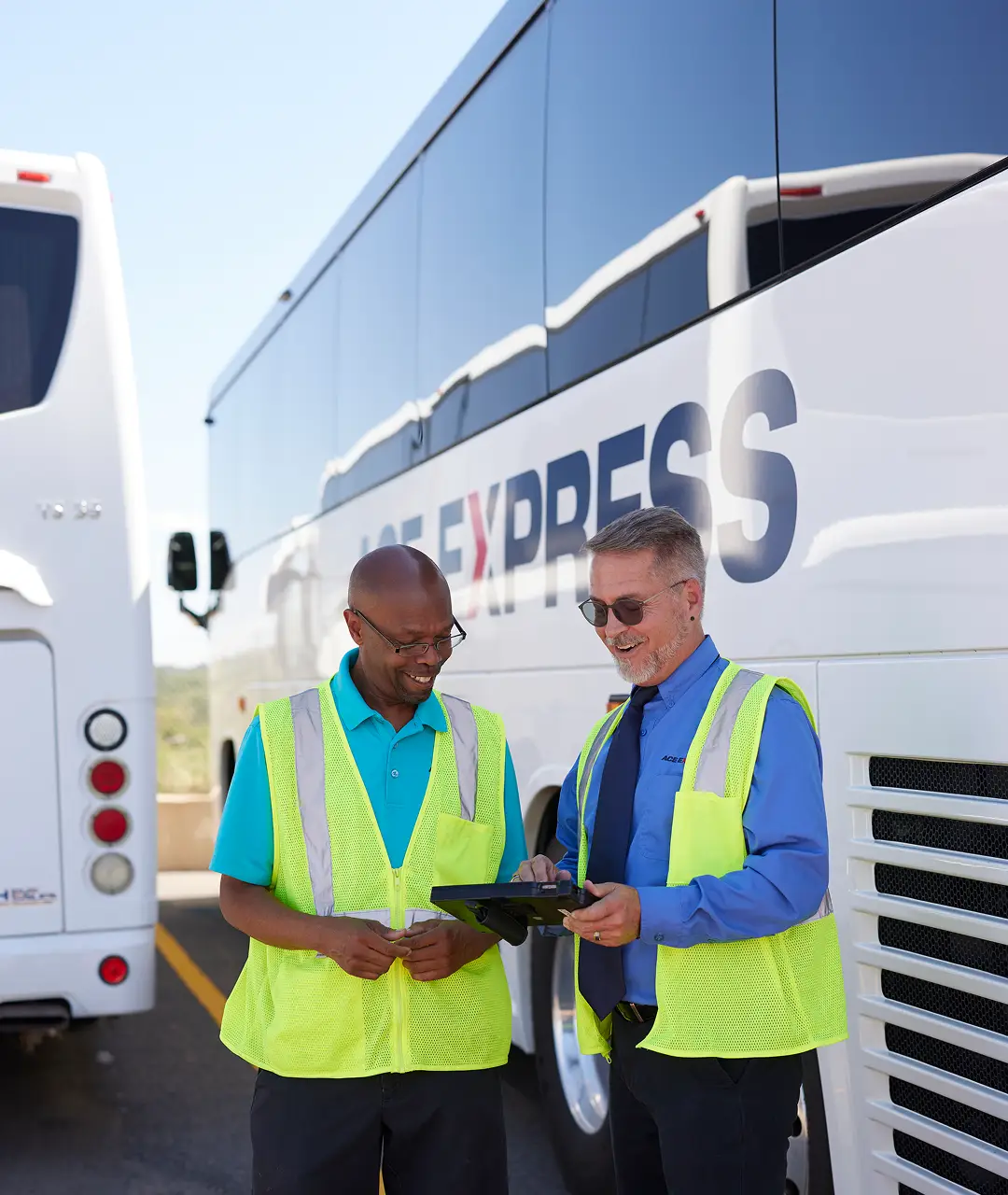 Two motorcoach staff members in safety vests discussing schedules outside the motorcoach.